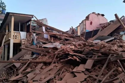 India Aid to Nepal: Indian and Nepal flags with damaged earthquake-hit buildings in the background representing reconstruction support.